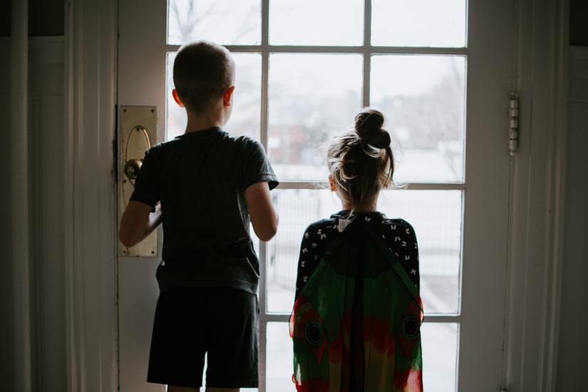 young brother and sister looking out glass door